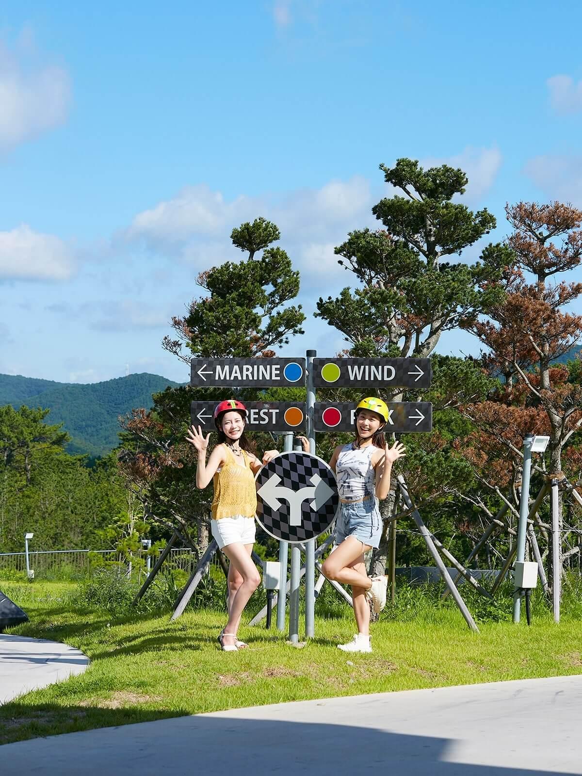 Two ladies pose for a photo in front of Luge track signage.