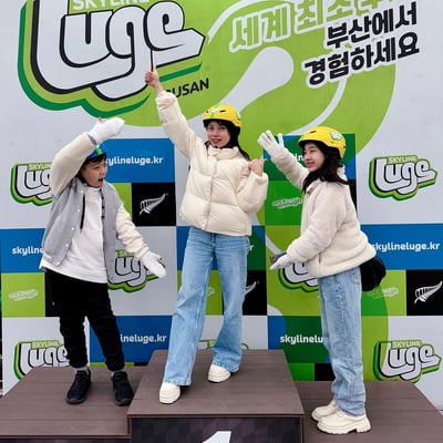 Three young kids stand on the Luge podium at the finish line.
