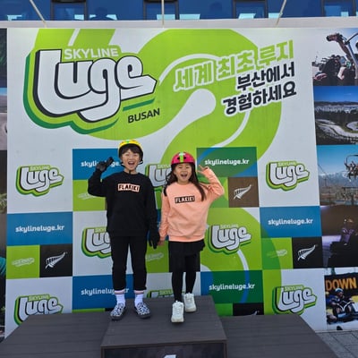 Two kids pose on the Luge podium at Skyline Luge Busan.
