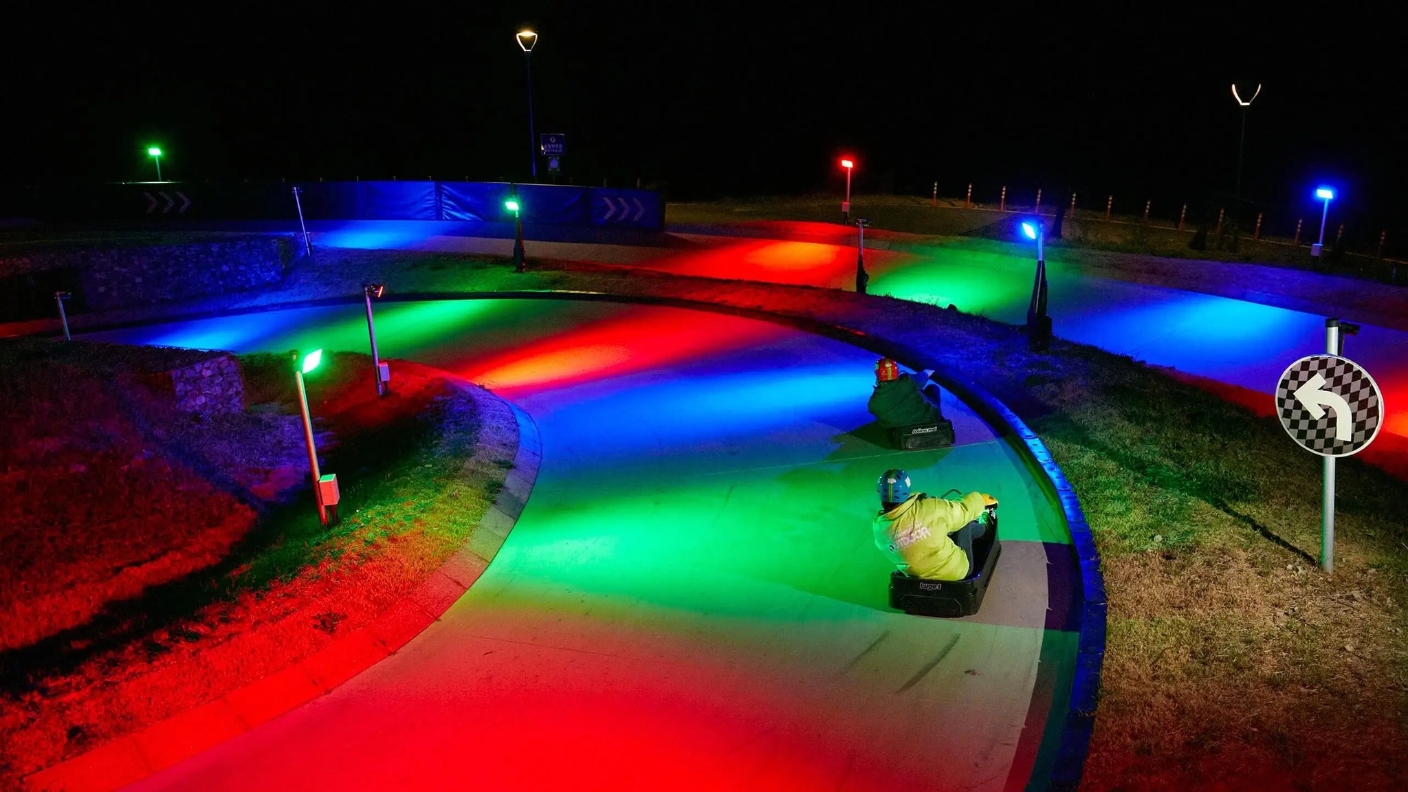 Two people riding around a corner on the Night Luge.